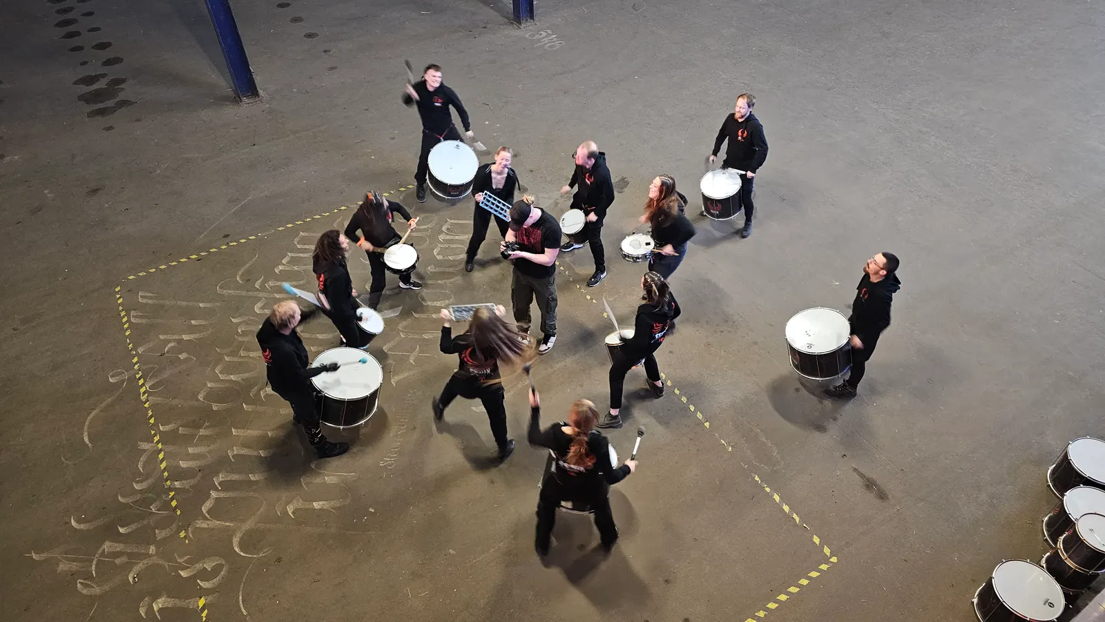Fenix Drums repeteert in een grote hal, gezien van bovenaf, met drummers die door elkaar lopen en spelen